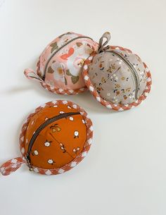 three small purses are sitting on a white surface, one is orange and the other is pink