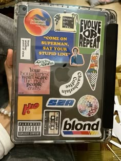 a person holding an apple laptop covered in stickers