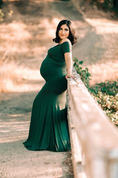 a pregnant woman leaning against a fence in a green dress with her hands on her hips