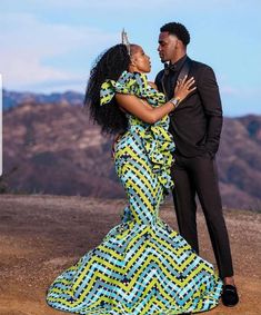 a man and woman dressed in african clothing posing for the camera with mountains in the background