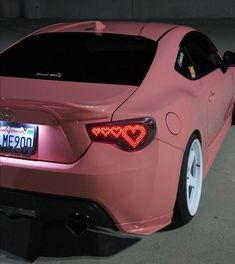 the back end of a pink sports car with its lights turned on and license plate