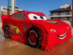 a red car made out of yarn on top of a wooden floor in front of a building