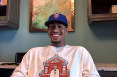 a young man wearing a baseball cap sitting in front of a painting on the wall