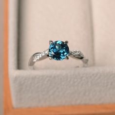 an engagement ring with a blue topazte surrounded by white diamonds in a box