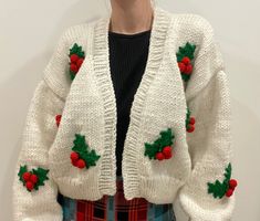 a woman wearing a white knitted christmas cardigan with holly and red berries on it