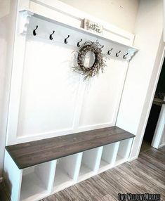 a white coat rack with hooks and a wreath on it next to a wooden bench