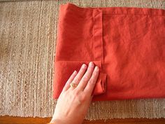 a woman is sewing on an orange piece of cloth with her hand and the edge of the fabric