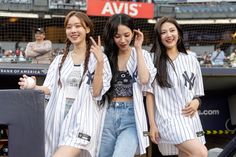 three girls are standing in the stands at a baseball game and one girl is holding her hands up