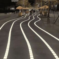 the lights are shining on the road in the city at night, with people walking down it