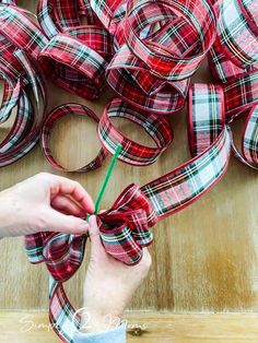 a person is cutting ribbon with scissors on a wooden table next to red and white plaid ribbons