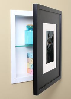 a black cat is looking at the camera from behind a shelf with some pictures on it