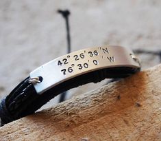 a personalized leather bracelet with coordinates and date engraved on the side, sitting on a piece of wood