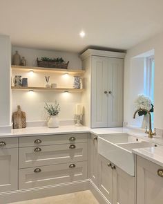 a kitchen with white cabinets and countertops has flowers in vases on the shelf