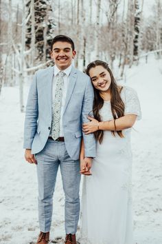 a man and woman standing next to each other on a snow covered field with trees in the background