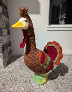 a crocheted turkey sitting on the ground next to a brick wall and window