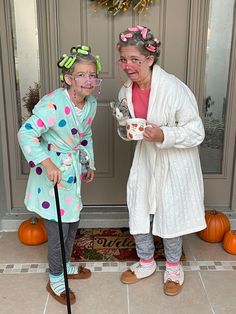 two older women standing next to each other in front of a door with pumpkins