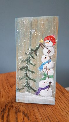 a glass block with three snowmen on it sitting on a table next to a pine tree