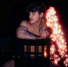 a man with tattoos sitting in front of a christmas tree