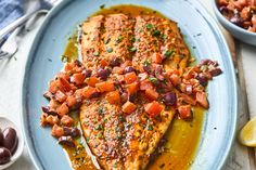 a plate topped with fish covered in sauce and garnished with olives next to a bowl of olives