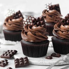 cupcakes with chocolate frosting and decorations on a white plate next to silverware