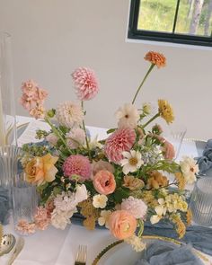 an arrangement of flowers in a vase on a table with plates and napkins around it