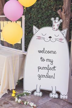 a welcome sign with balloons in the shape of a cat and a crown on top