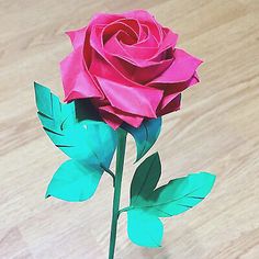 a pink rose with green leaves in a vase on a wooden table, ready to be used as a centerpiece