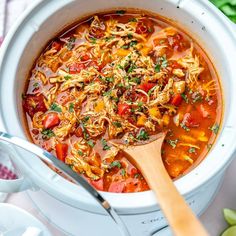 a white pot filled with chicken tortilla soup and a wooden spoon in it