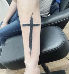 a person sitting on a chair with a cross tattoo on their arm and the leg