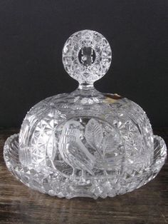 a glass covered dish with a bird on it's lid and an oval handle