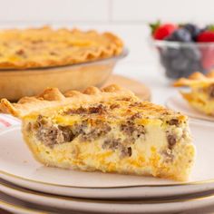 a slice of sausage and cheese quiche on a plate with berries in the background