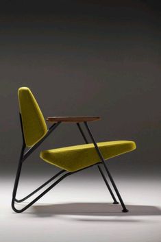 a yellow chair sitting next to a wooden table on top of a gray floor in front of a black wall