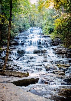 a waterfall in the middle of a forest with lots of water running down it's sides