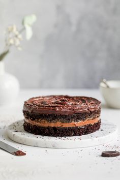 a chocolate cake sitting on top of a white plate next to a vase with flowers