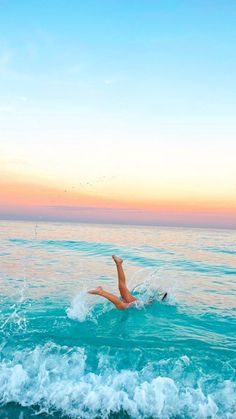 a woman laying on top of a surfboard in the middle of the ocean at sunset