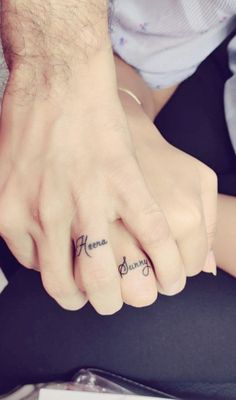 two people with tattoos on their fingers holding each other's hands and one has the word