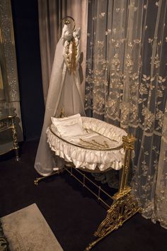 a baby crib in front of a curtained window with white curtains and gold trim