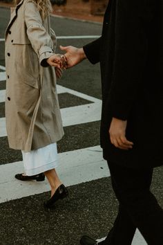 a man and woman walking across a cross walk holding each other's hands in the street