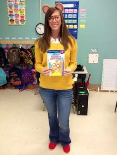 a woman holding up a book in front of her face while standing in a classroom