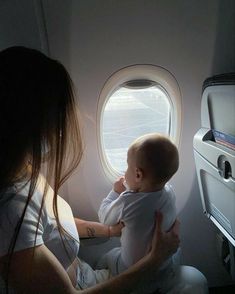 a woman holding a baby while looking out an airplane window