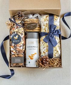 an open gift box filled with nuts, crackers, and chocolates next to a blue ribbon