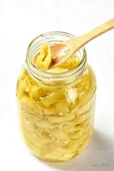 a jar filled with pickles on top of a white table next to a wooden spoon