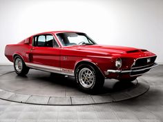 an old red mustang sitting on top of a black and white circular floored area