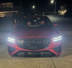 the front end of a red car parked in a parking lot at night