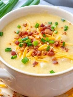 a close up of a bowl of soup with cheese and green onions on the side