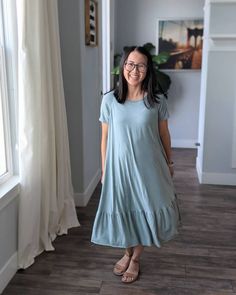 a woman standing in front of a window with her hands in her pockets and smiling