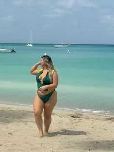 a woman in a green and yellow bathing suit on the beach with boats in the background