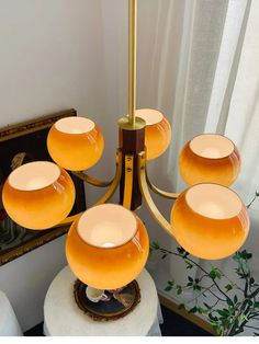 a chandelier with five orange glass bowls on it and a mirror in the background