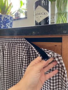 a person holding a knife in front of a counter with flowers on it and a gingham cloth draped around the edge