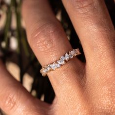 a woman's hand with a diamond ring on top of her finger and flowers in the background